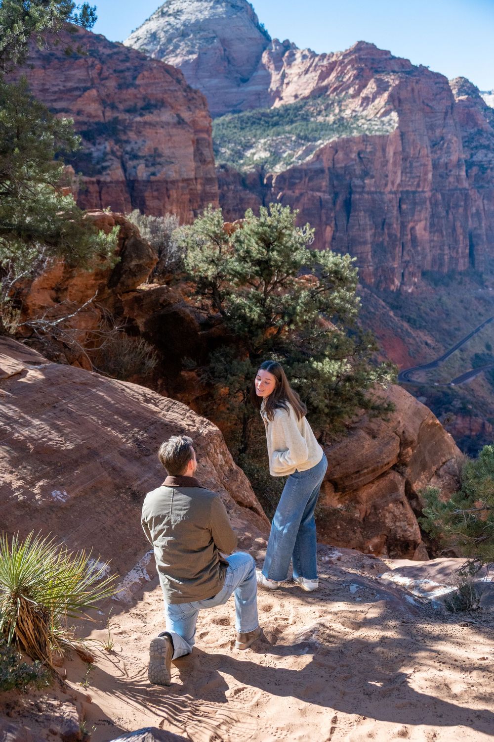 Couple sharing romantic marriage proposal moment on scenic Zion National Park red rock hiking trail.