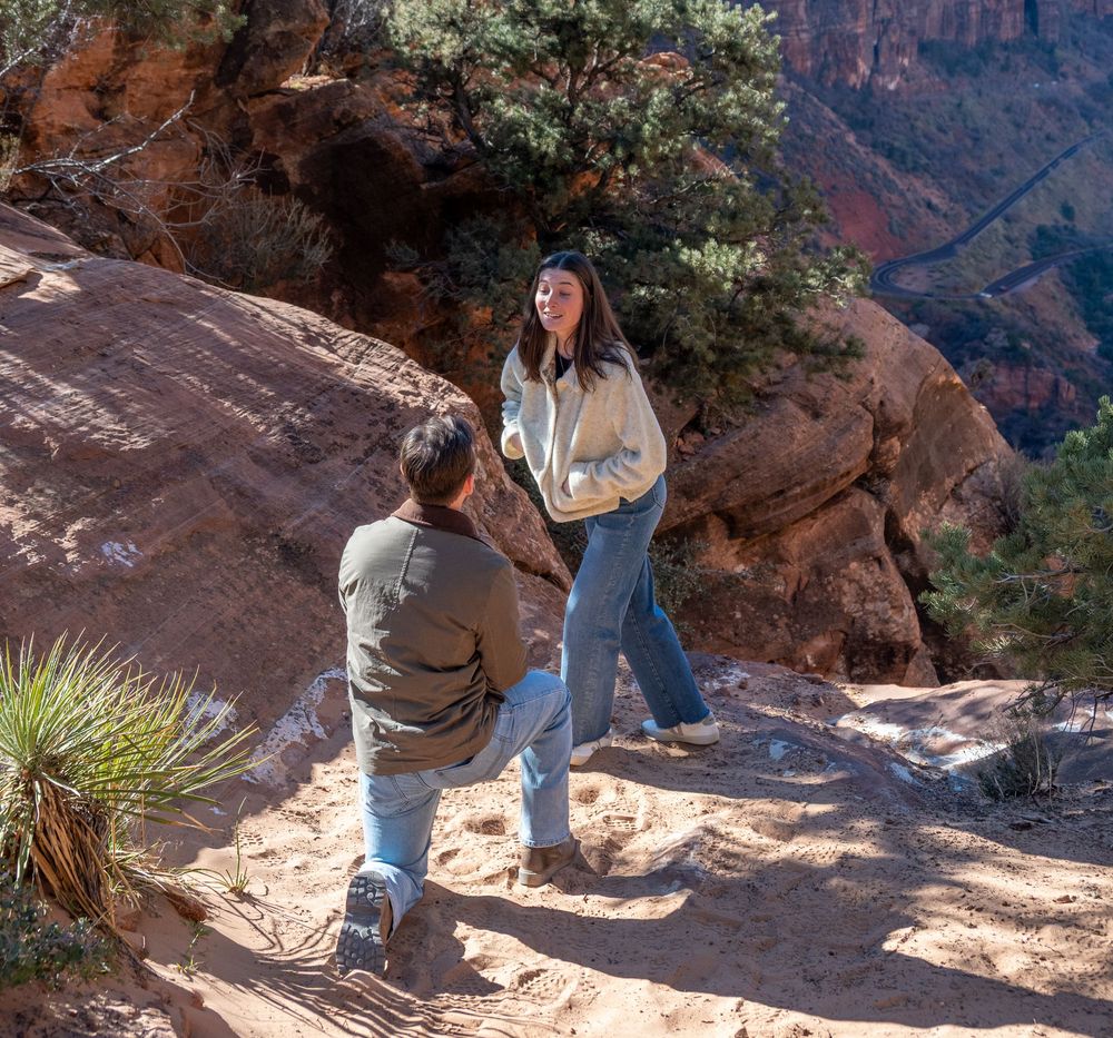 Man proposing on one knee to his surprised girlfriend on a red rock canyon trail.