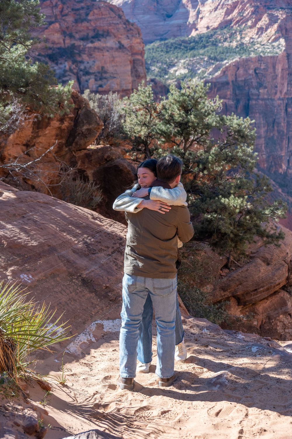 Happy couple hugging after marriage proposal on scenic red rock overlook at Zion National Park.