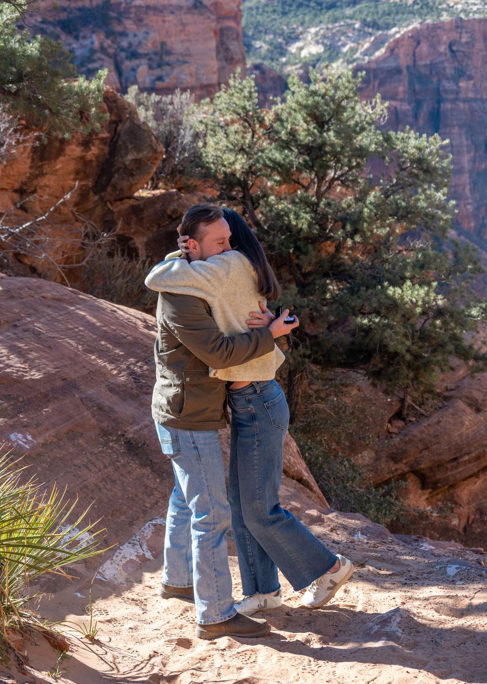 Newly engaged couple celebrating with joyful embrace on Zion National Park red canyon trail.