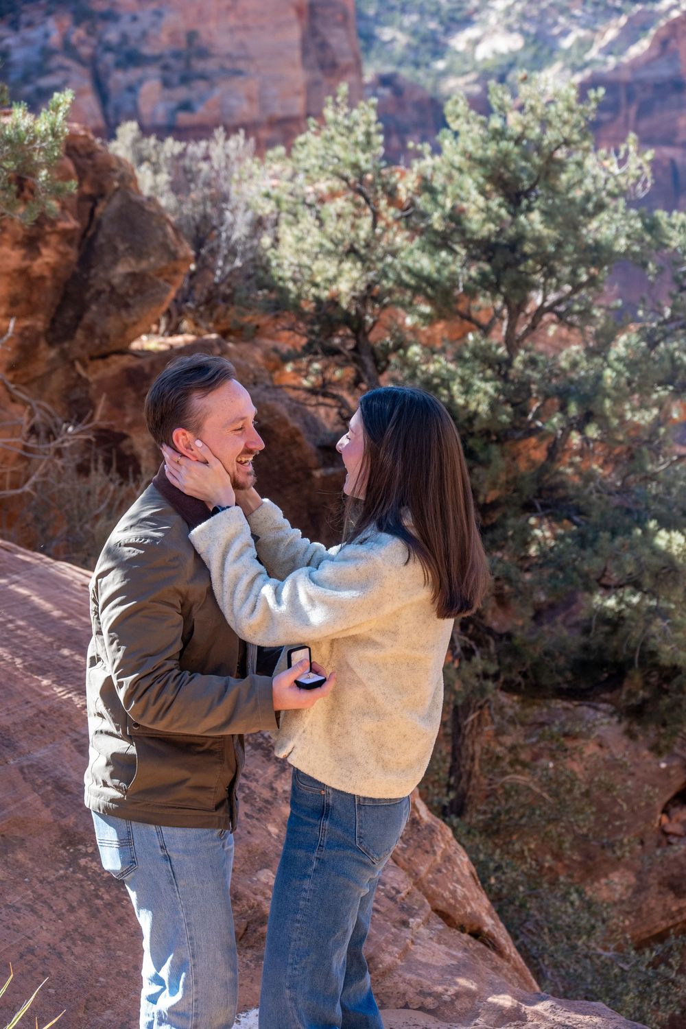 Joyful couple embracing during a marriage proposal on red rock trails in Zion National Park.