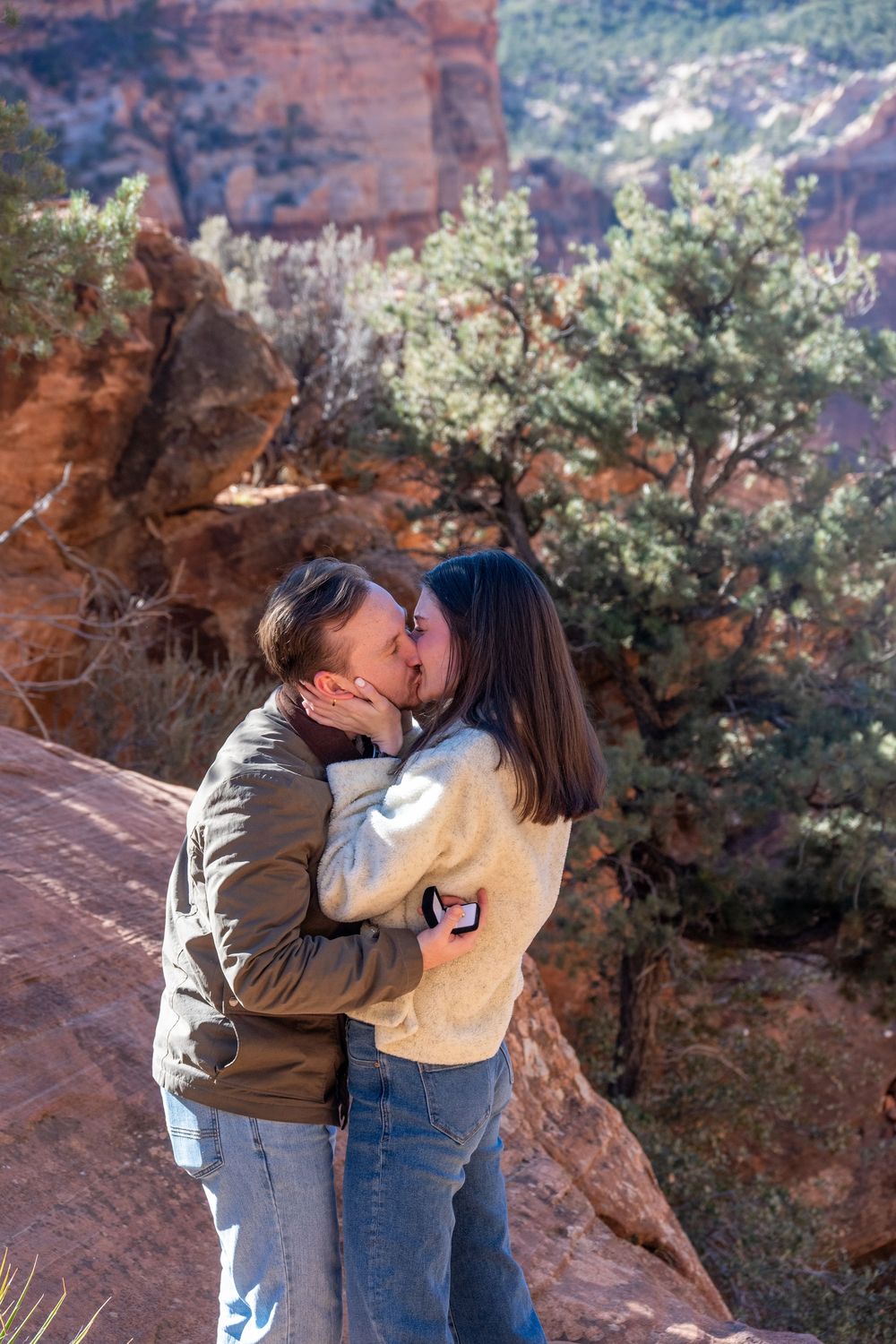 Newly engaged couple sharing a kiss against stunning red rock canyon backdrop in Zion National Park.