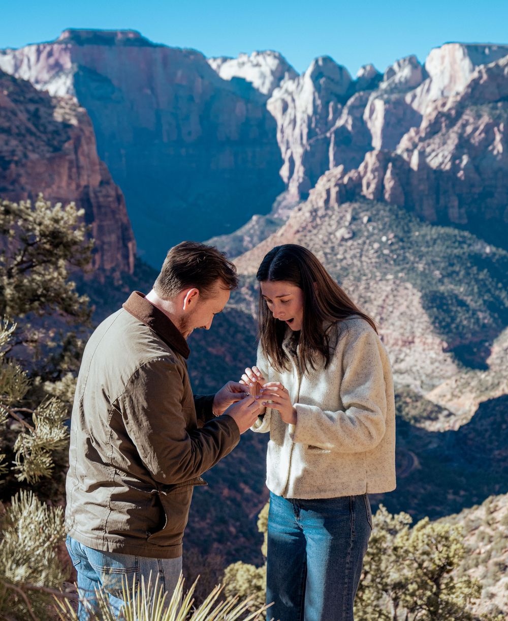 Romantic marriage proposal with man placing ring on womans finger at Zion National Park summit.