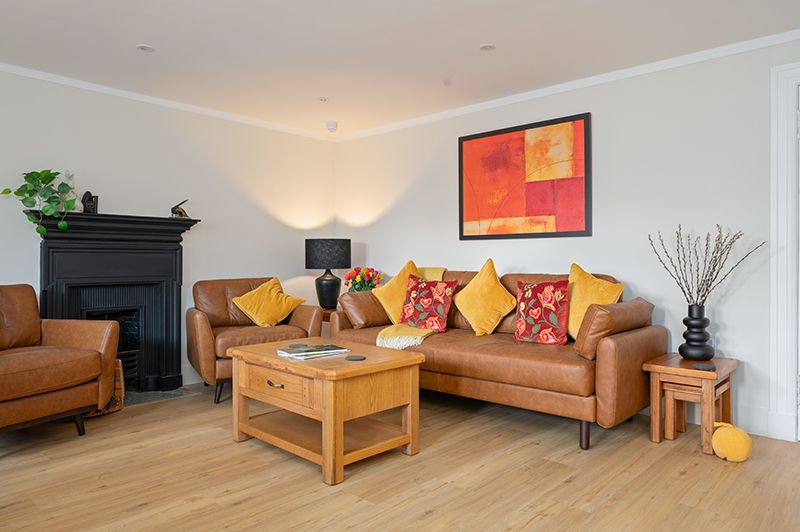 Modern living room interior with brown leather sofa, wooden coffee table and colorful throw pillows against white walls.
