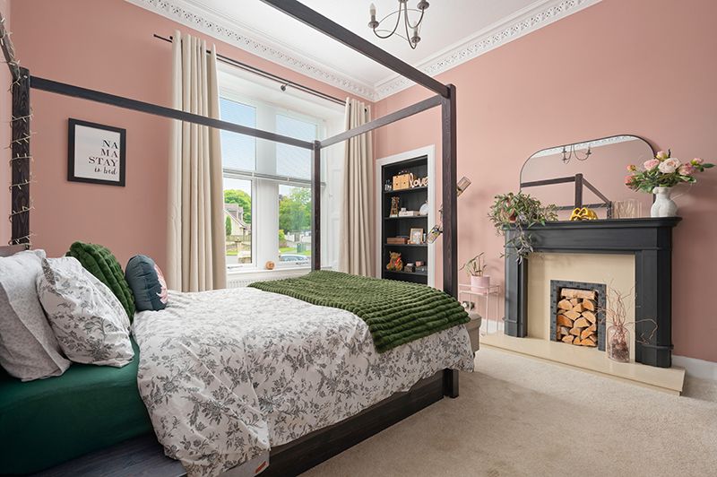 Modern bedroom interior with pink walls, ornate crown molding, and gray floral bedding in a sunlit space.