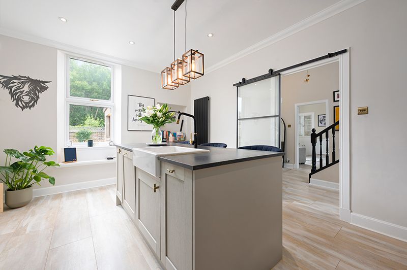 Modern white kitchen with light wood flooring, stainless steel appliances, and copper pendant lights over a center island.