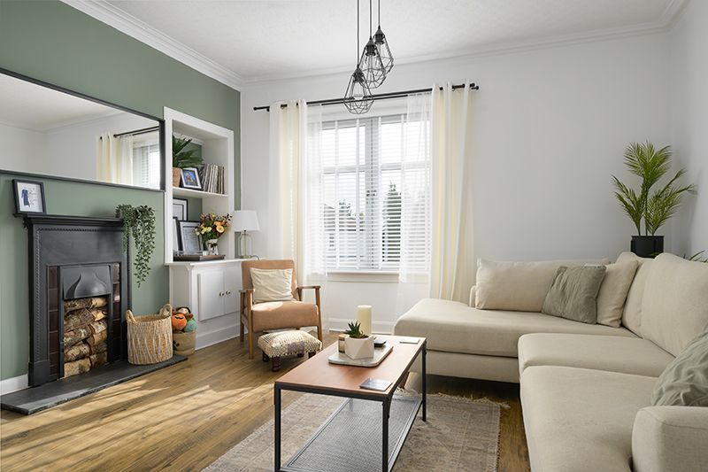 Modern living room with sage green accent wall, cream sectional sofa, and industrial coffee table on hardwood floors.