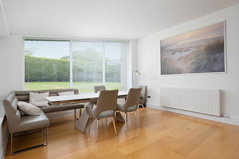 Modern dining area with built-in bench seating, wooden table, chairs and large landscape artwork in bright room with windows.