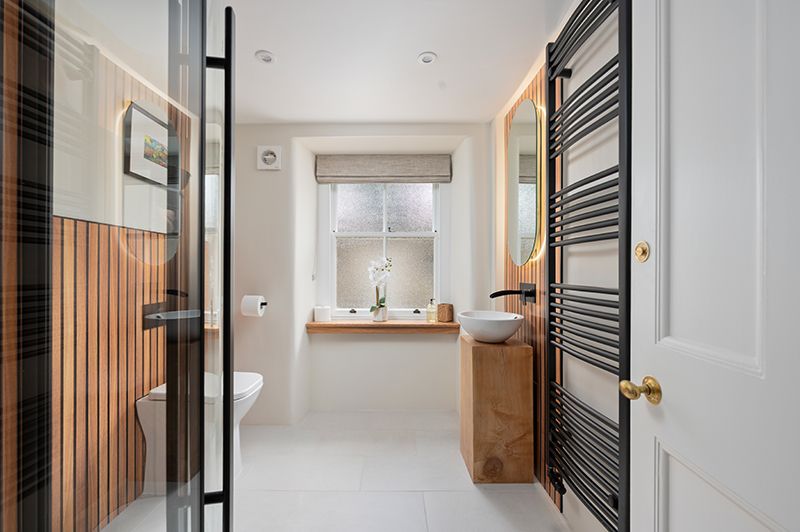 Modern bathroom interior with wood accents features black ladder towel rack and white walls.