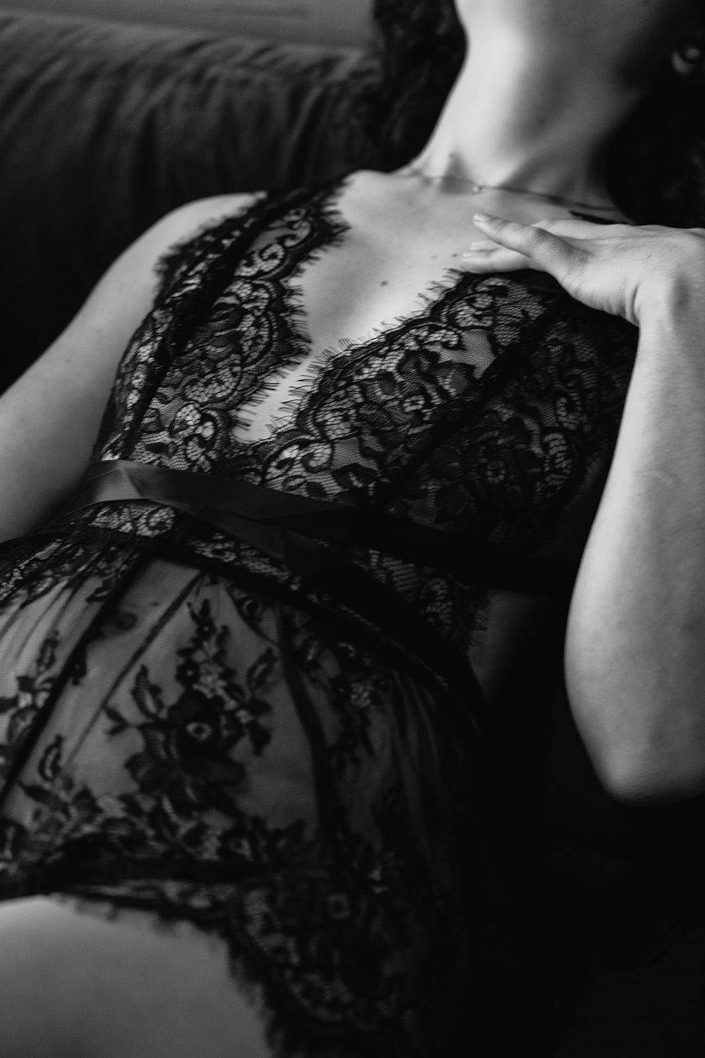 Black and white close-up of a woman in sheer black lace teddy lingerie reclining gracefully.