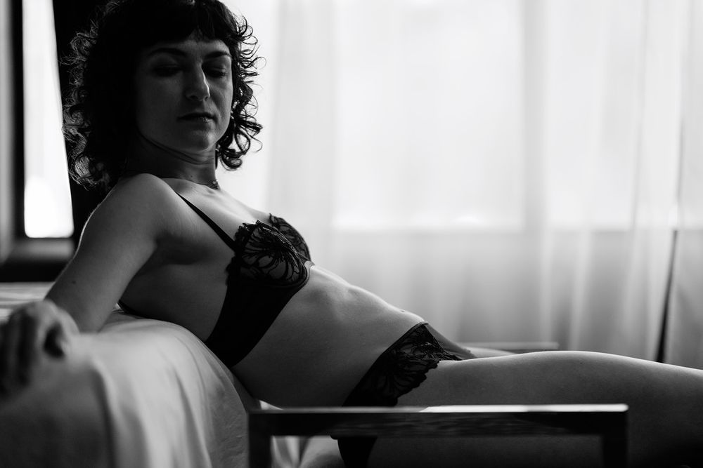 Black and white boudoir portrait of curly-haired woman reclining in black lace lingerie.