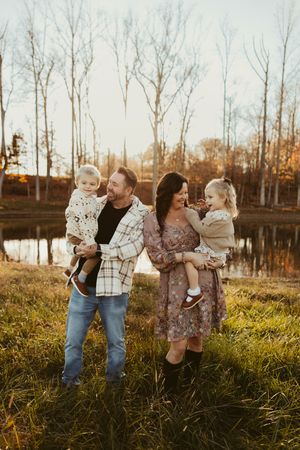 Happy family of four with two young children pose by a golden sunset pond in autumn landscape.