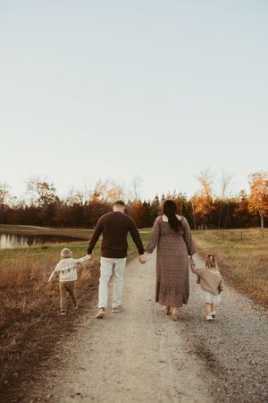 Family of four walking away down a gravel path beside a pond during a beautiful autumn sunset.