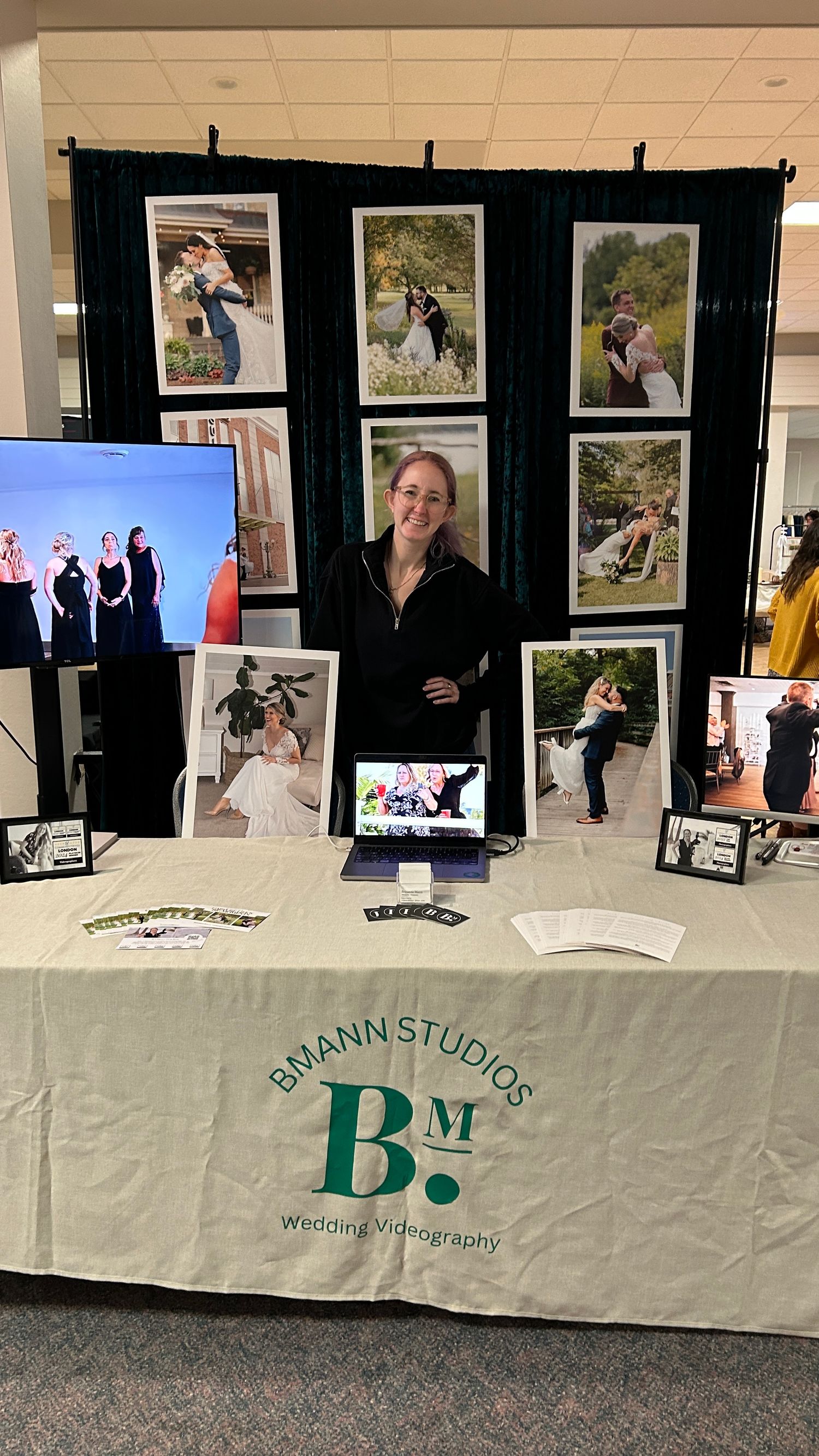 Photography display booth at an event showcasing wedding photos on black panels with a branded white tablecloth.