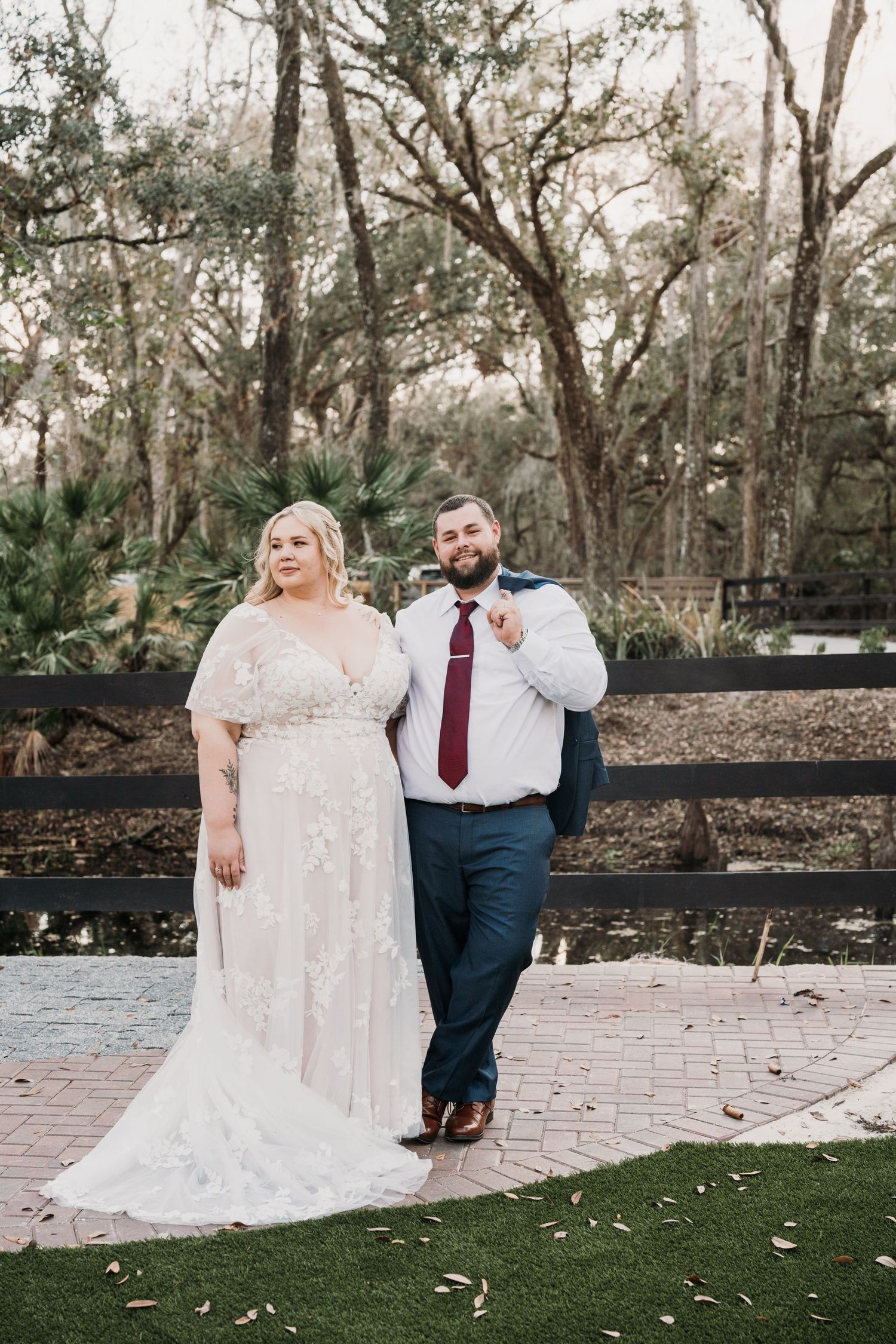 A couple poses together on a brick patio surrounded by trees during their outdoor wedding photo session.