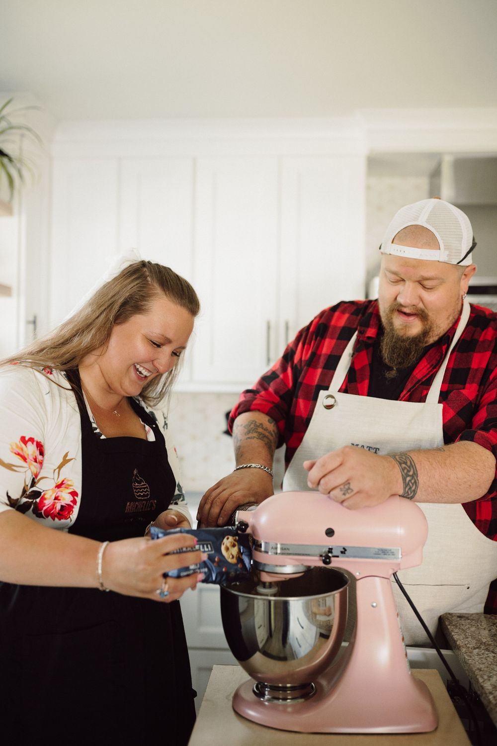 A couple bakes together using a pink stand mixer in a modern white kitchen.