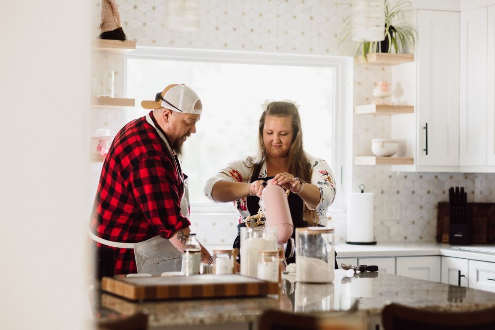 A bright, modern kitchen scene with two people baking together near a window.