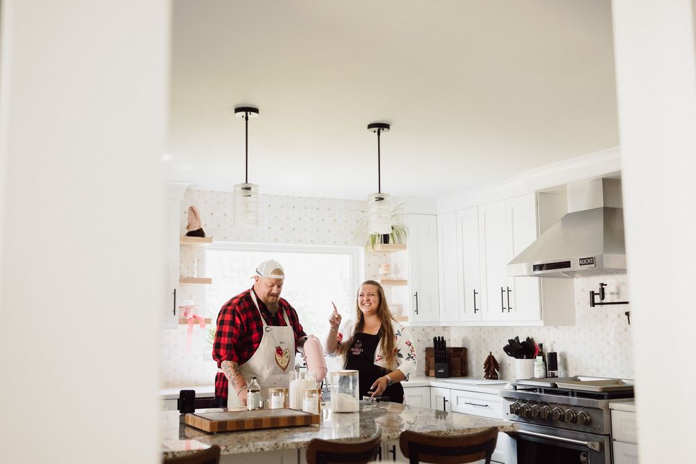Modern white kitchen with pendant lights and people baking together.