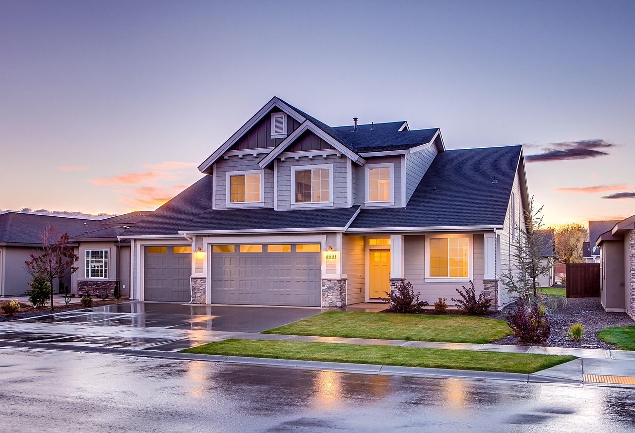 Beautiful two-story craftsman style house with grey siding and white trim illuminated at sunset with wet driveway.