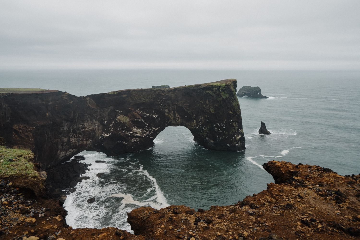 A stunning natural rock arch frames the ocean view along a dramatic rugged coastal cliff.
