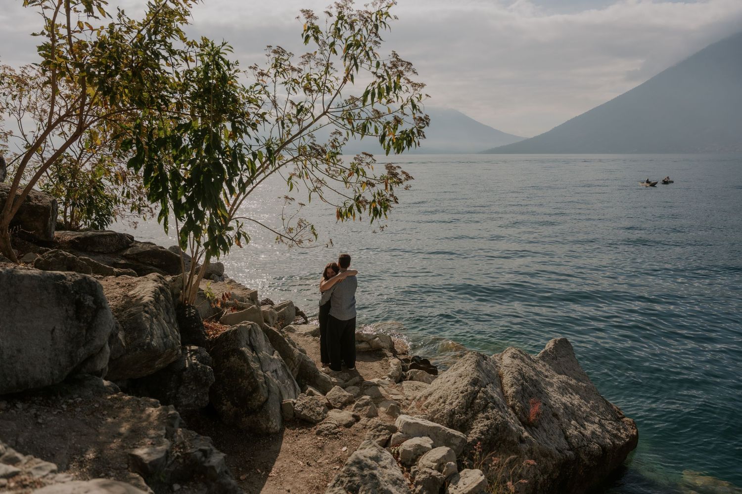 Panoramic view of a tranquil lake surrounded by misty mountains and rocky shoreline with eucalyptus trees.