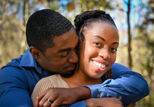 A loving couple embraces outdoors while sharing a tender moment against a natural wooded background.