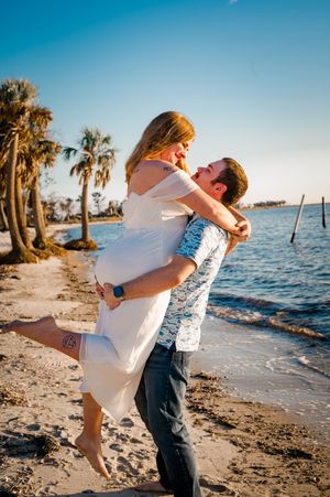 A romantic couple embraces on a tropical beach at sunset with palm trees and ocean in the background.