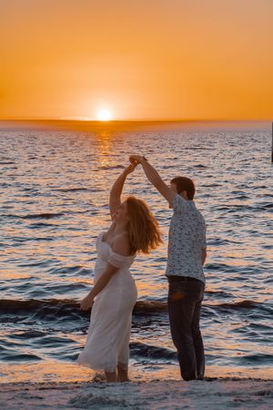 A couple dances together on the beach during a romantic golden sunset over the ocean.