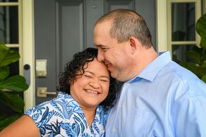 A couple in a blue patterned dress and light blue shirt share an intimate moment outdoors.