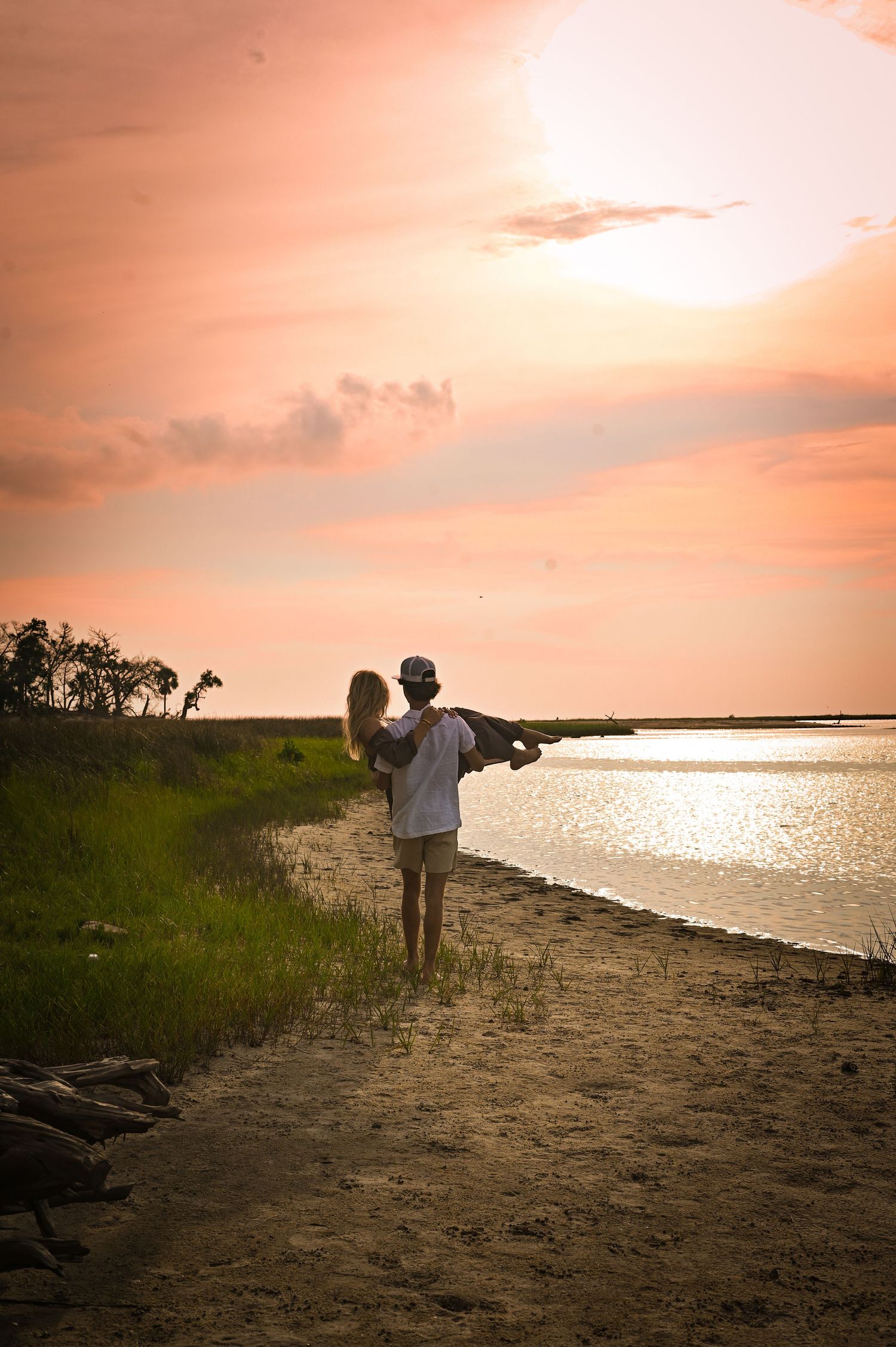Two silhouettes stand together on a beach shoreline during a golden sunset over calm waters.