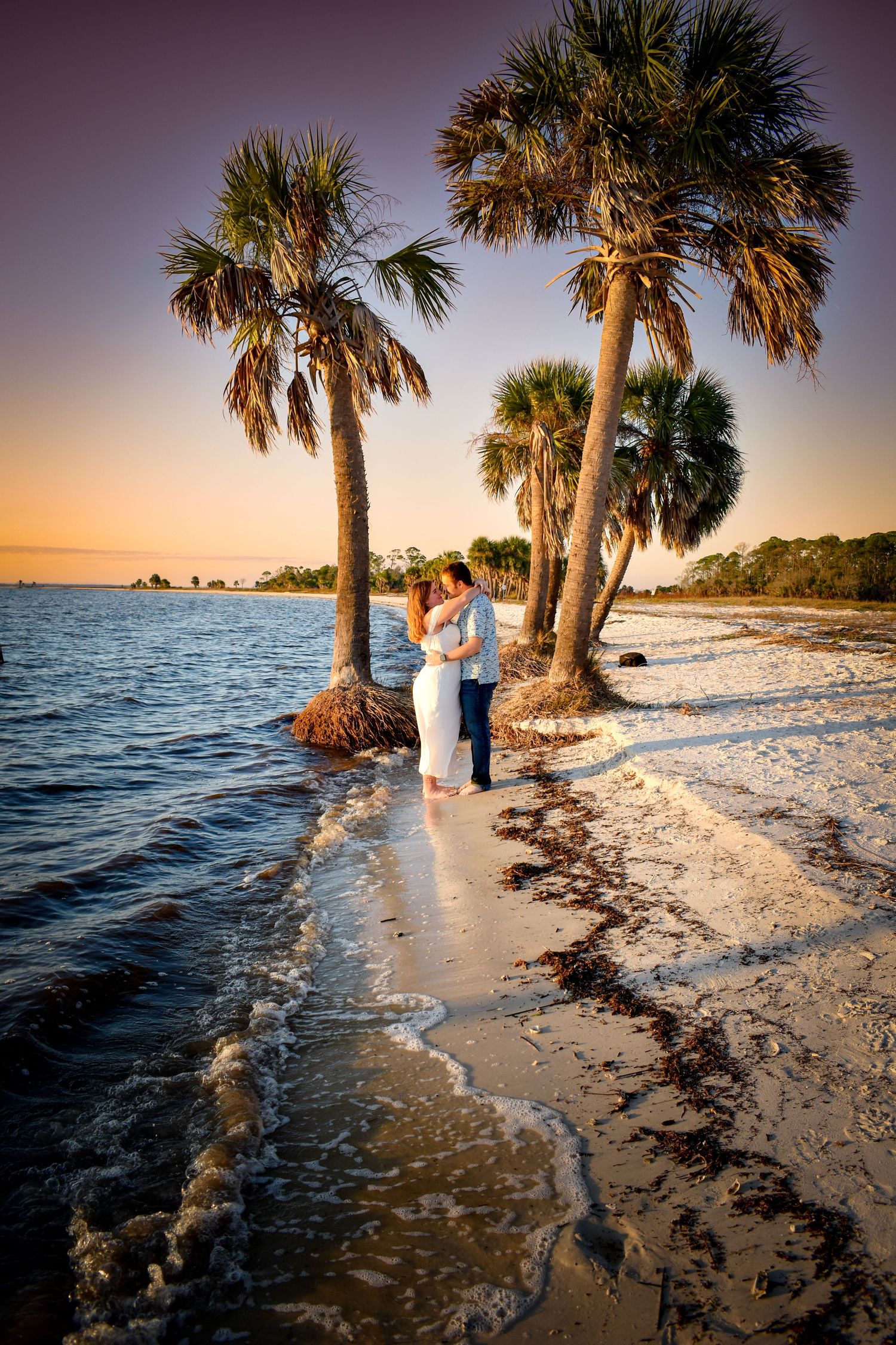 Palm trees line a sandy beach at sunset as gentle waves lap the shoreline during a tranquil evening photoshoot.