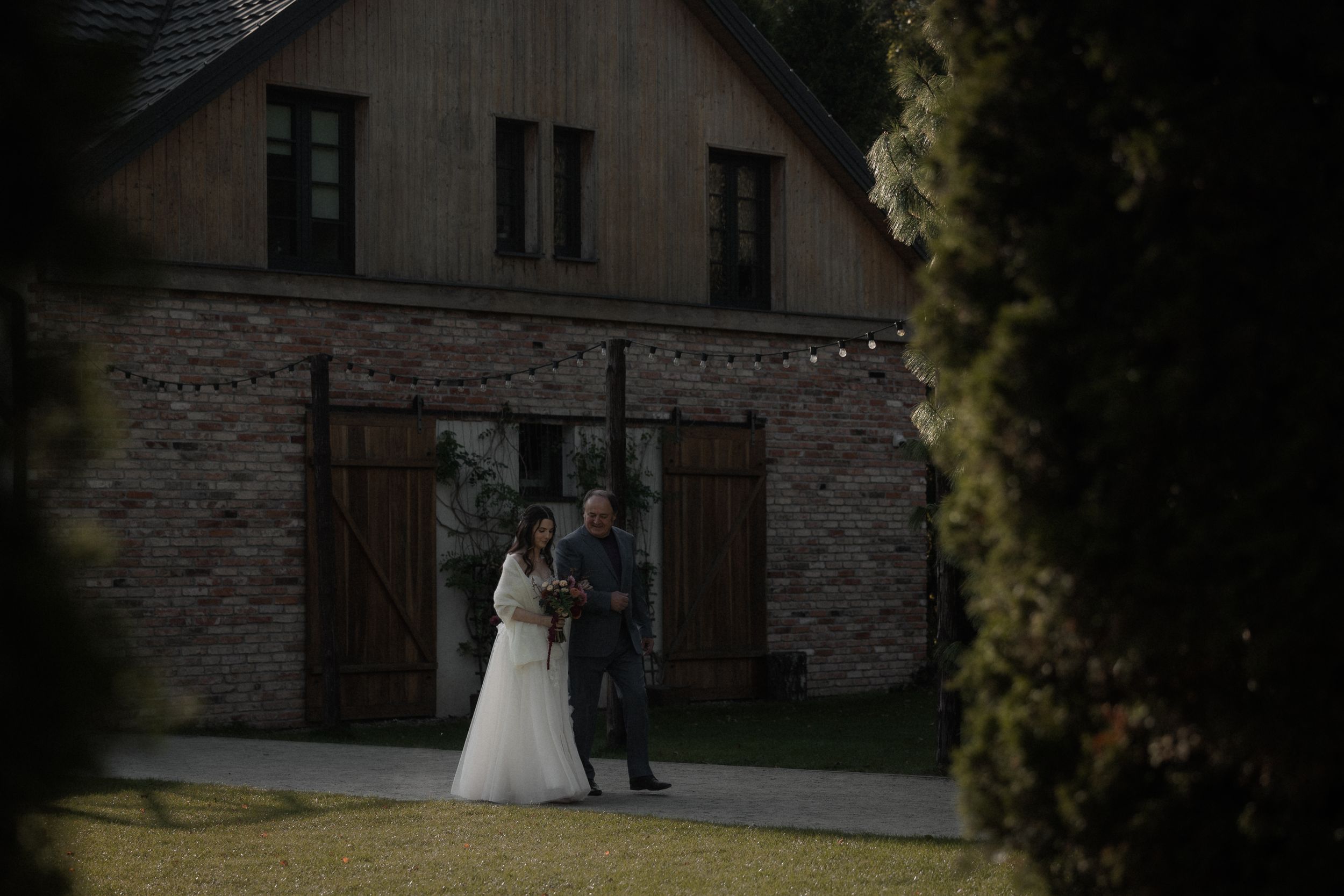A bride and groom walk along a stone building exterior during an elegant wedding photoshoot.