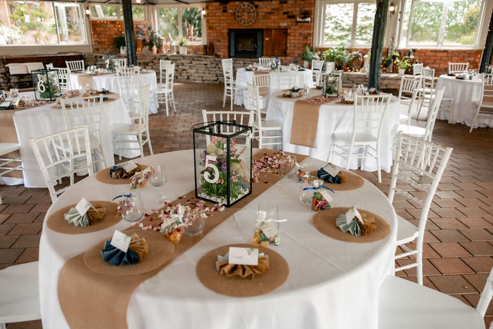 Rustic wedding reception venue decorated with white chairs and natural wood tables in a barn setting.