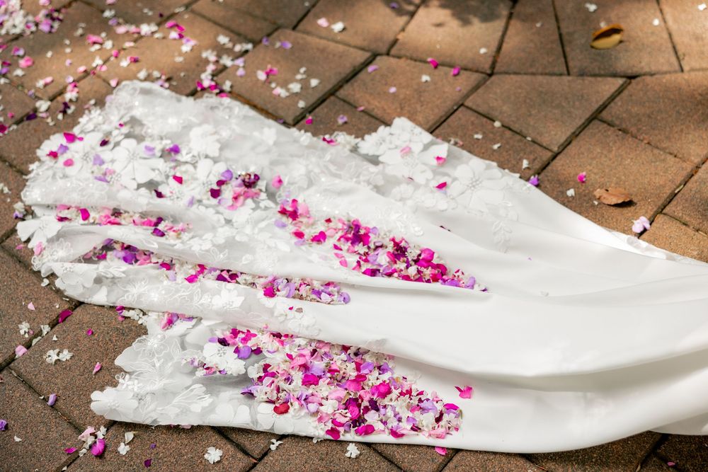 White wedding dress train decorated with scattered pink flower petals on terracotta tiles.