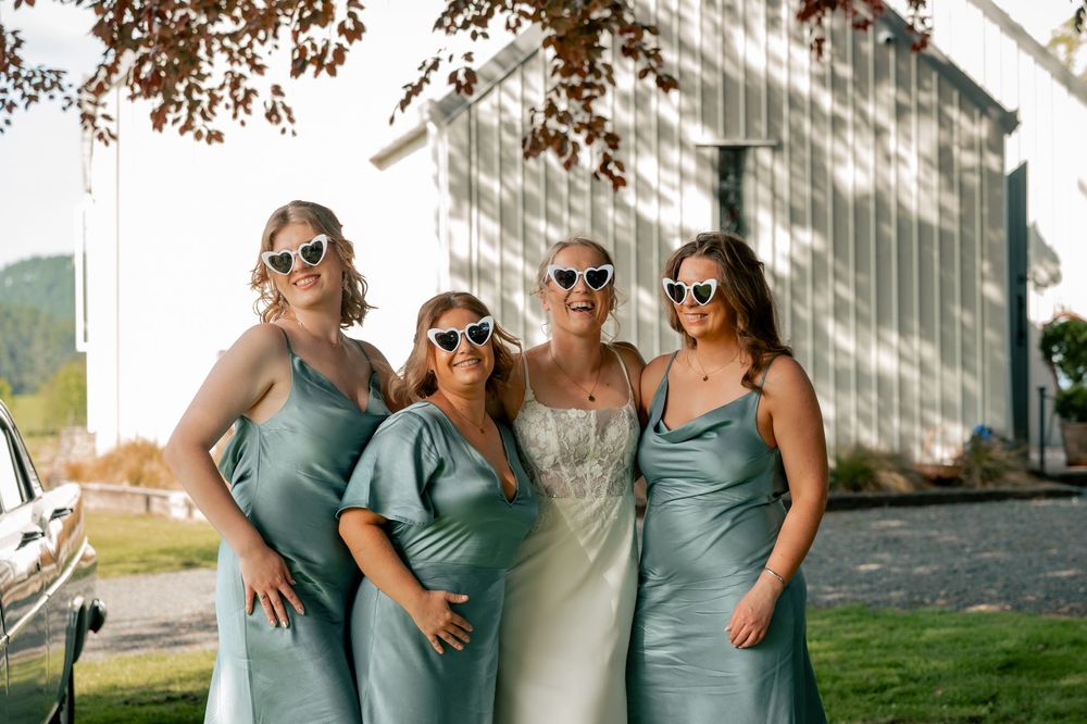 Wedding party members in sage green and white attire posing together in natural sunlight.