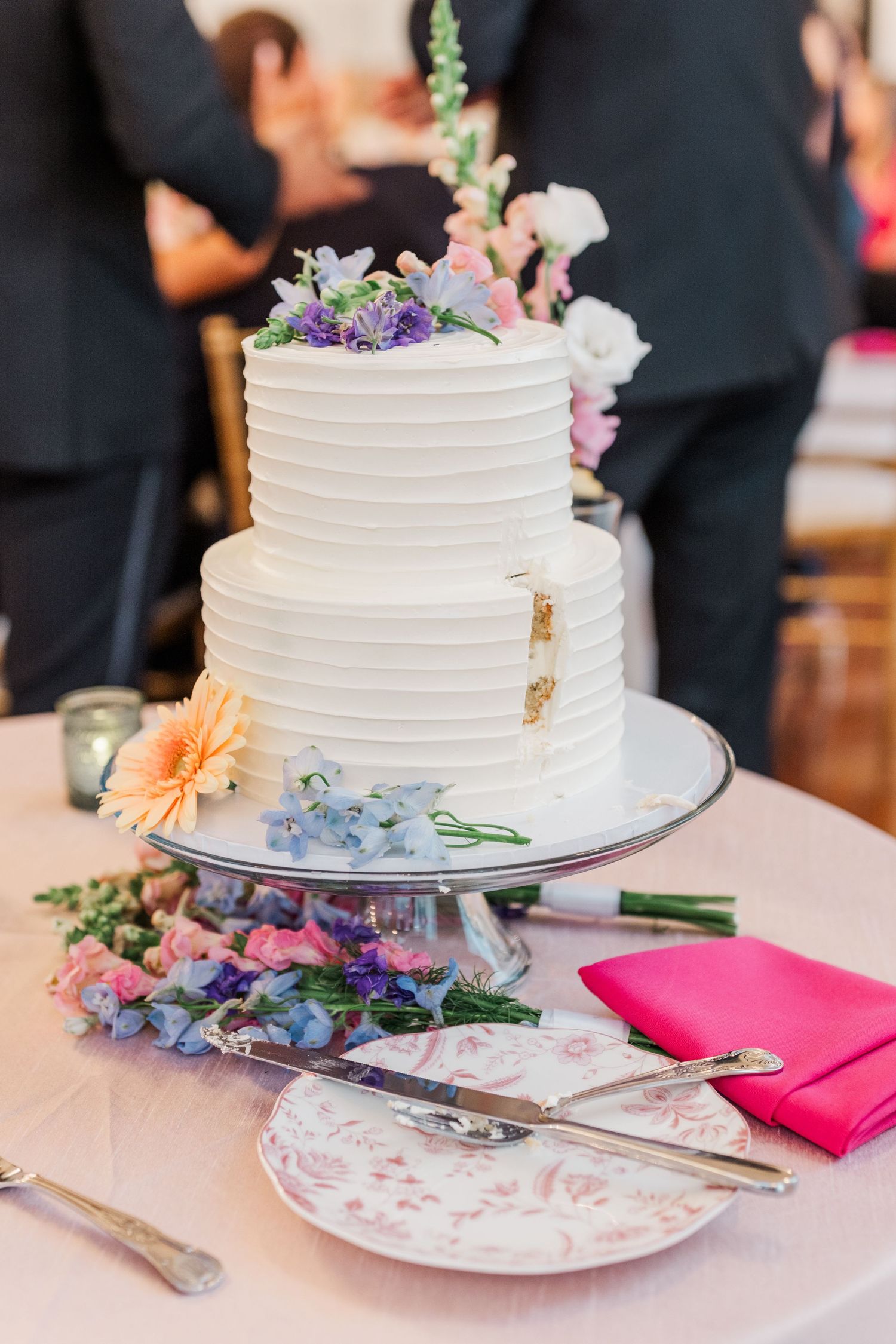 Elegant two-tier white wedding cake decorated with fresh flowers and pink napkins on display.