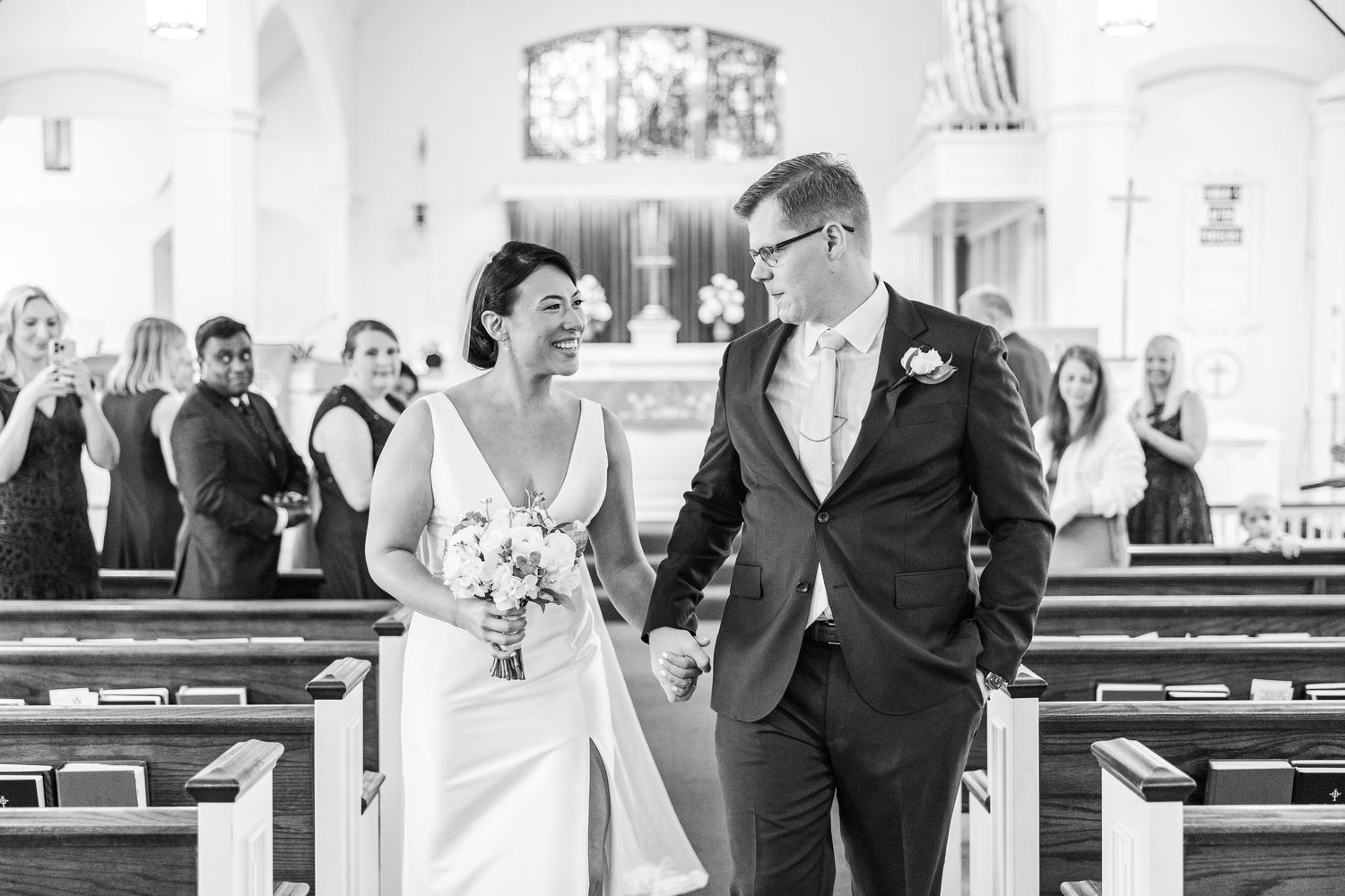 Black and white photo of couple sharing joyful moment in church aisle.