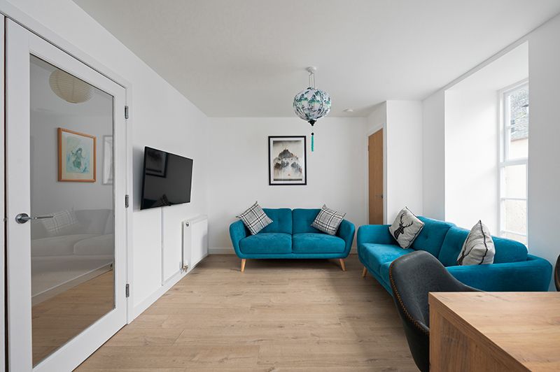 Modern white living room interior with teal accent couch and wooden floors features minimalist decor and natural lighting.