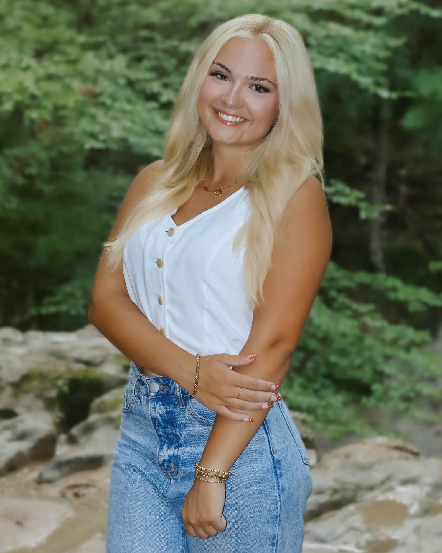 A person in denim and white top poses playfully against a wooded background.