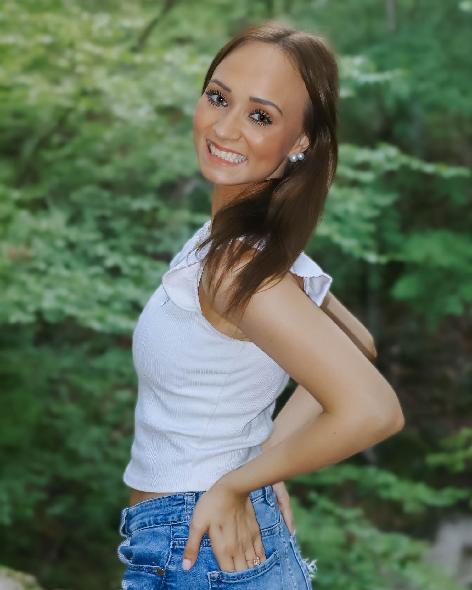 Playful outdoor portraits in white top and denim against green background.