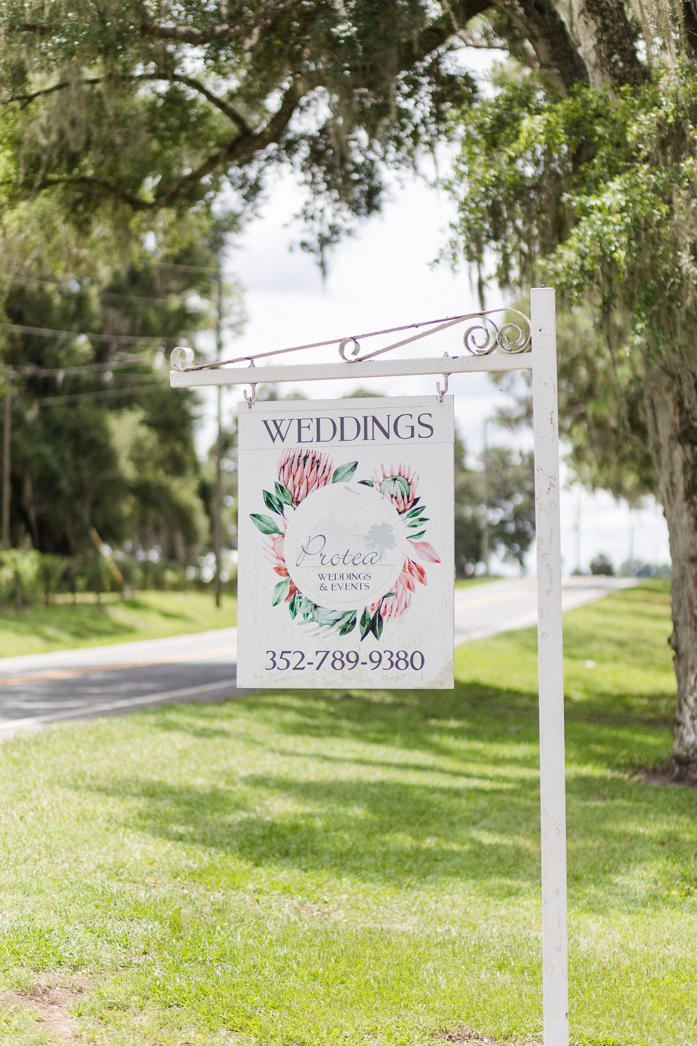 Elegant wedding venue sign with floral wreath design hanging from decorative post.