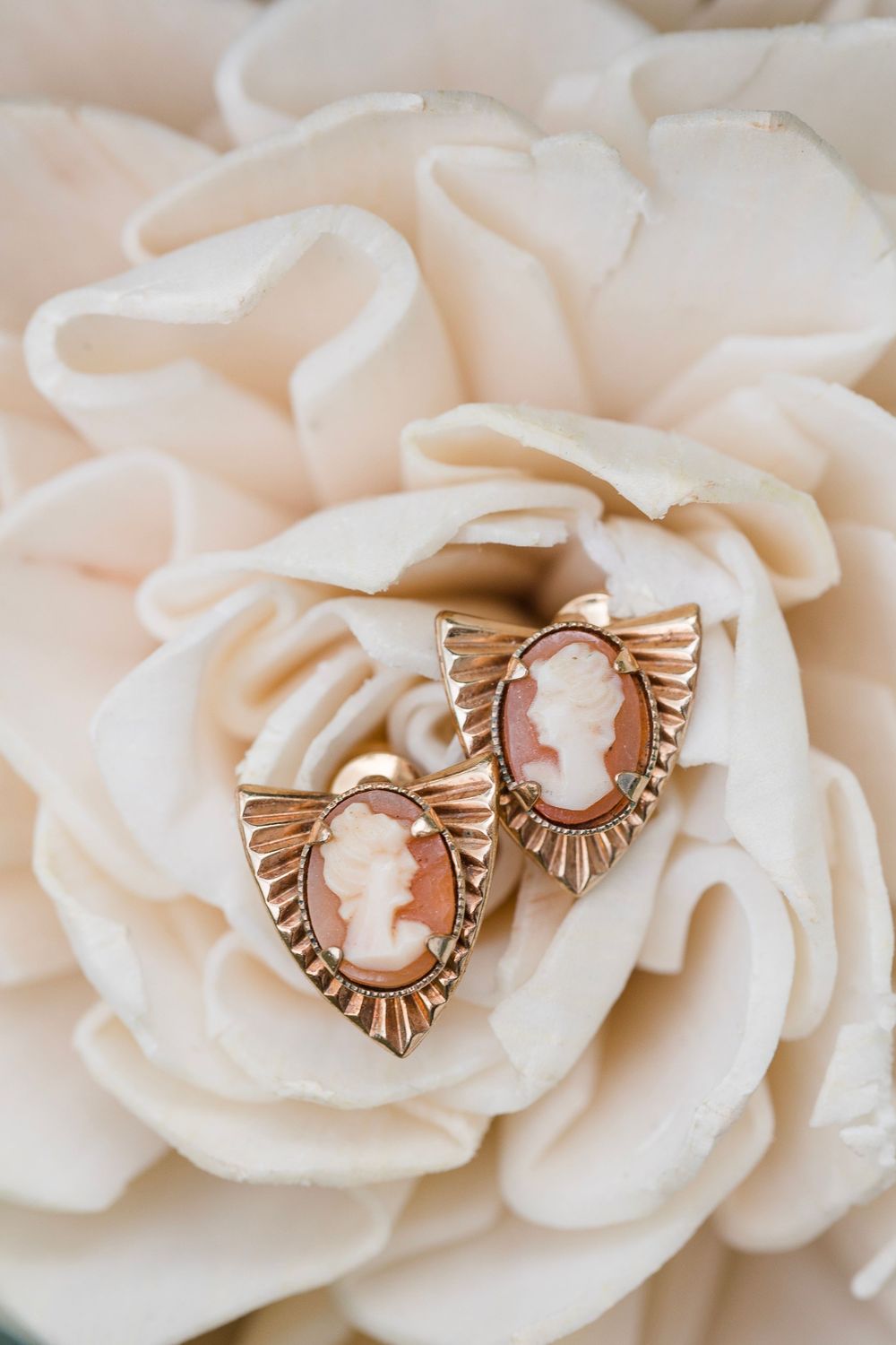 Vintage-style gold cameo earrings resting on delicate white rose petals.