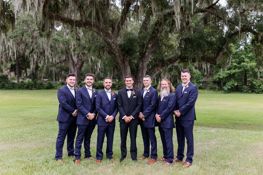 Wedding party in navy suits and dresses posed together under Spanish moss trees.