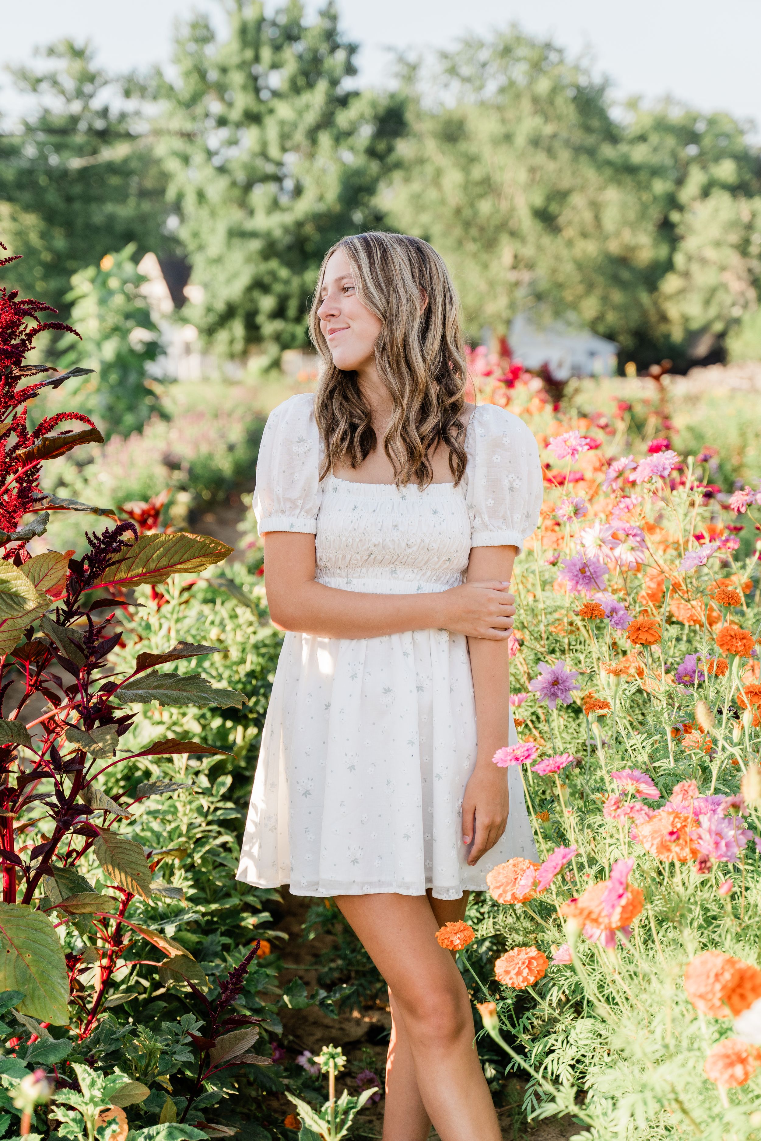 White eyelet dress contrasts beautifully with colorful dahlias and zinnias in a lush flower garden setting.