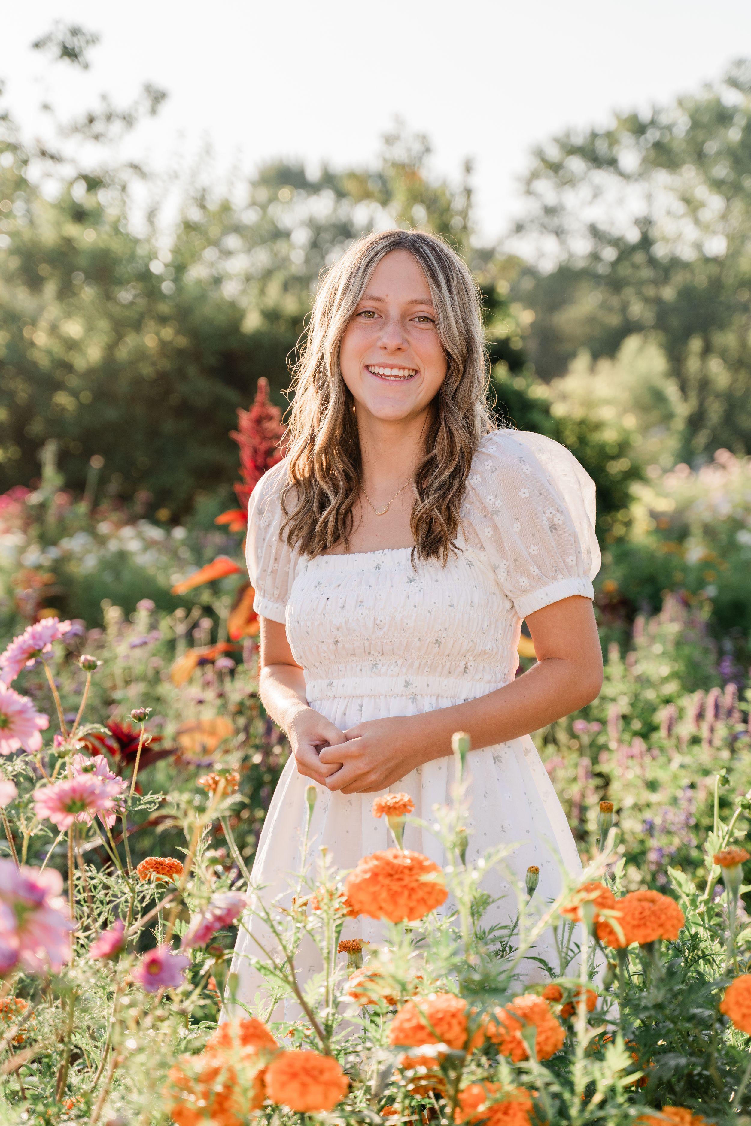 A white sundress stands out among vibrant orange and pink flowers in a summer garden during golden hour.