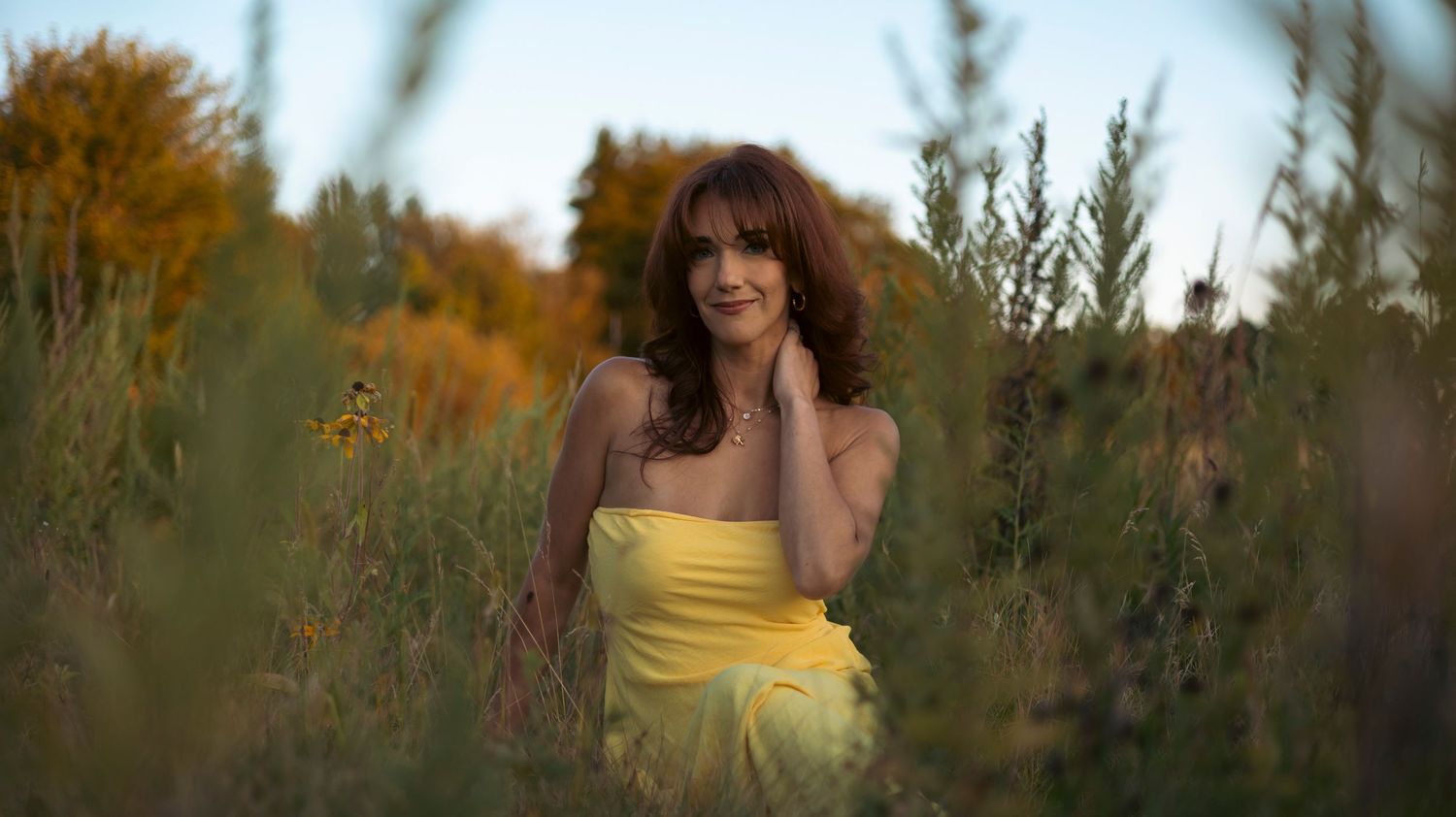 A person in a yellow sundress walks through a golden field at sunset with warm backlighting.