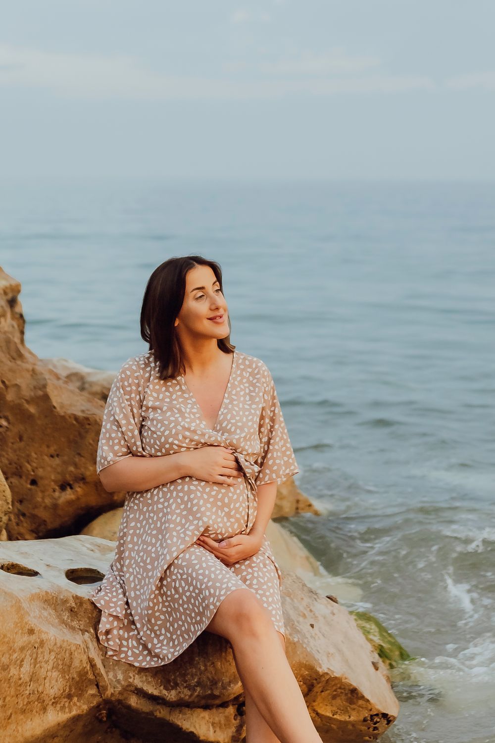 Maternity portrait of an expectant mother sitting on coastal rocks at golden hour in Southbourne Beach, Dorset