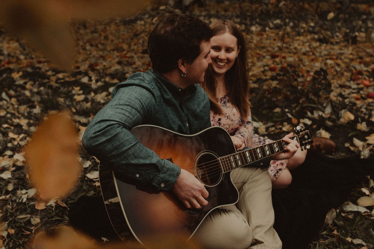 Couple sharing intimate moments during an autumn engagement photoshoot with acoustic guitar in fallen leaves.