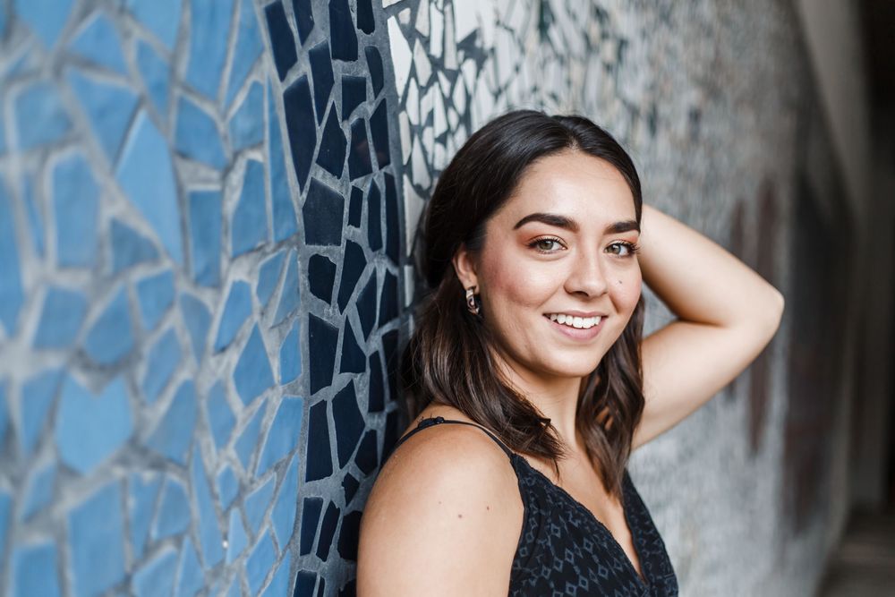 A woman in a black dress poses against a gray wall for a portrait photo session.