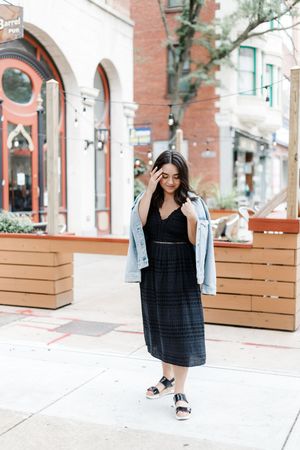 Lifestyle photoshoot with black dress and denim jacket near brick storefronts with wooden benches.